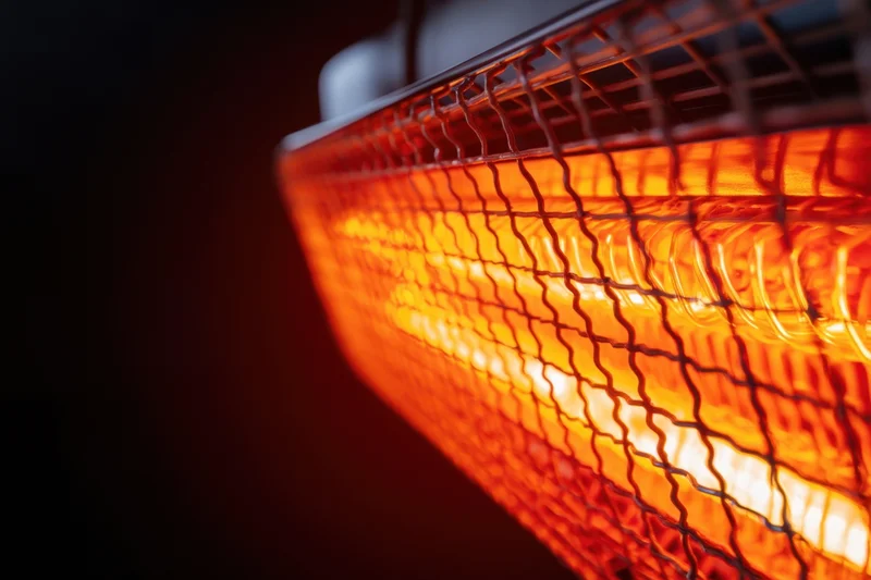 Close-up of glowing infrared heater with metal grid against dark background