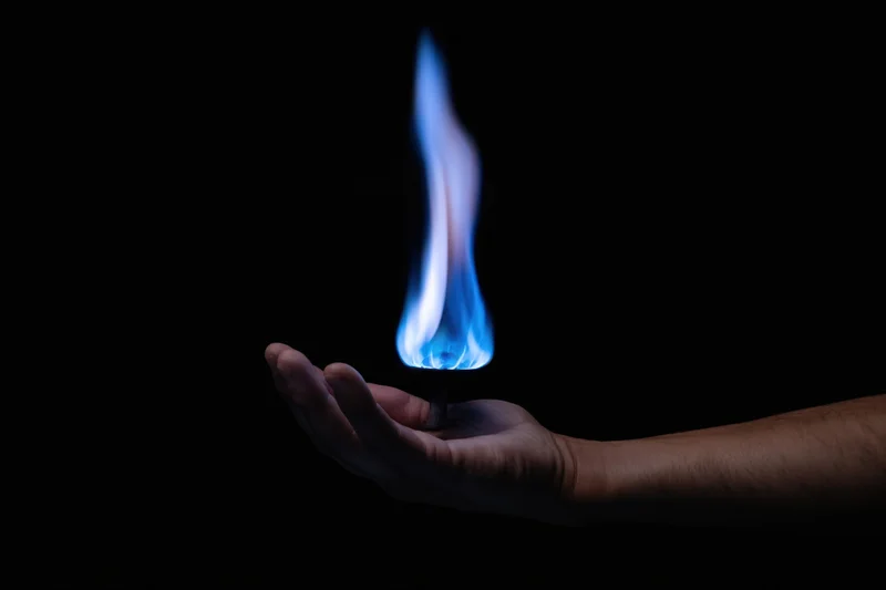 Hand holding a blue flame against a dark background
