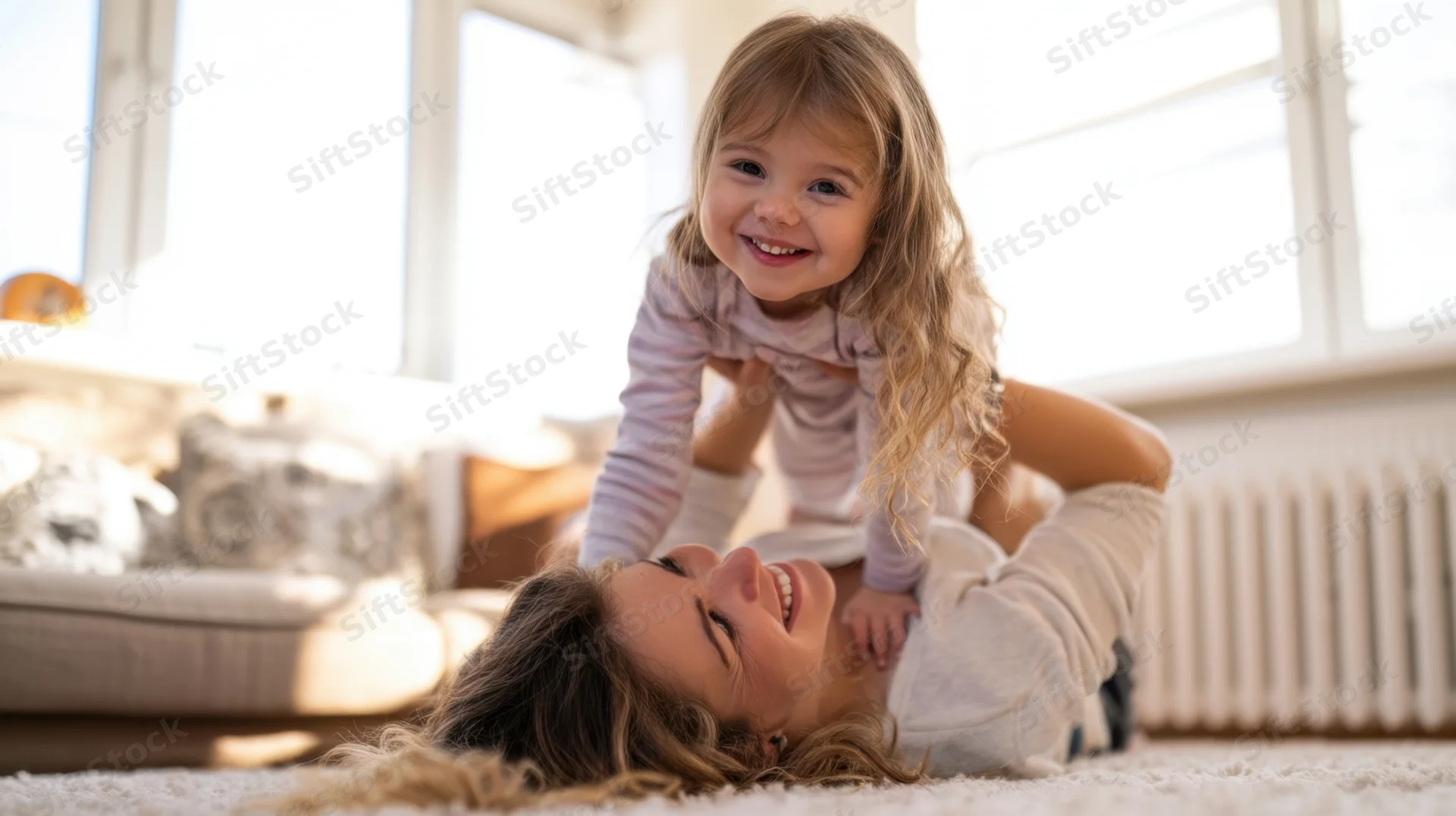 Mother lying on floor laughing with daughter playing on her chest in living room