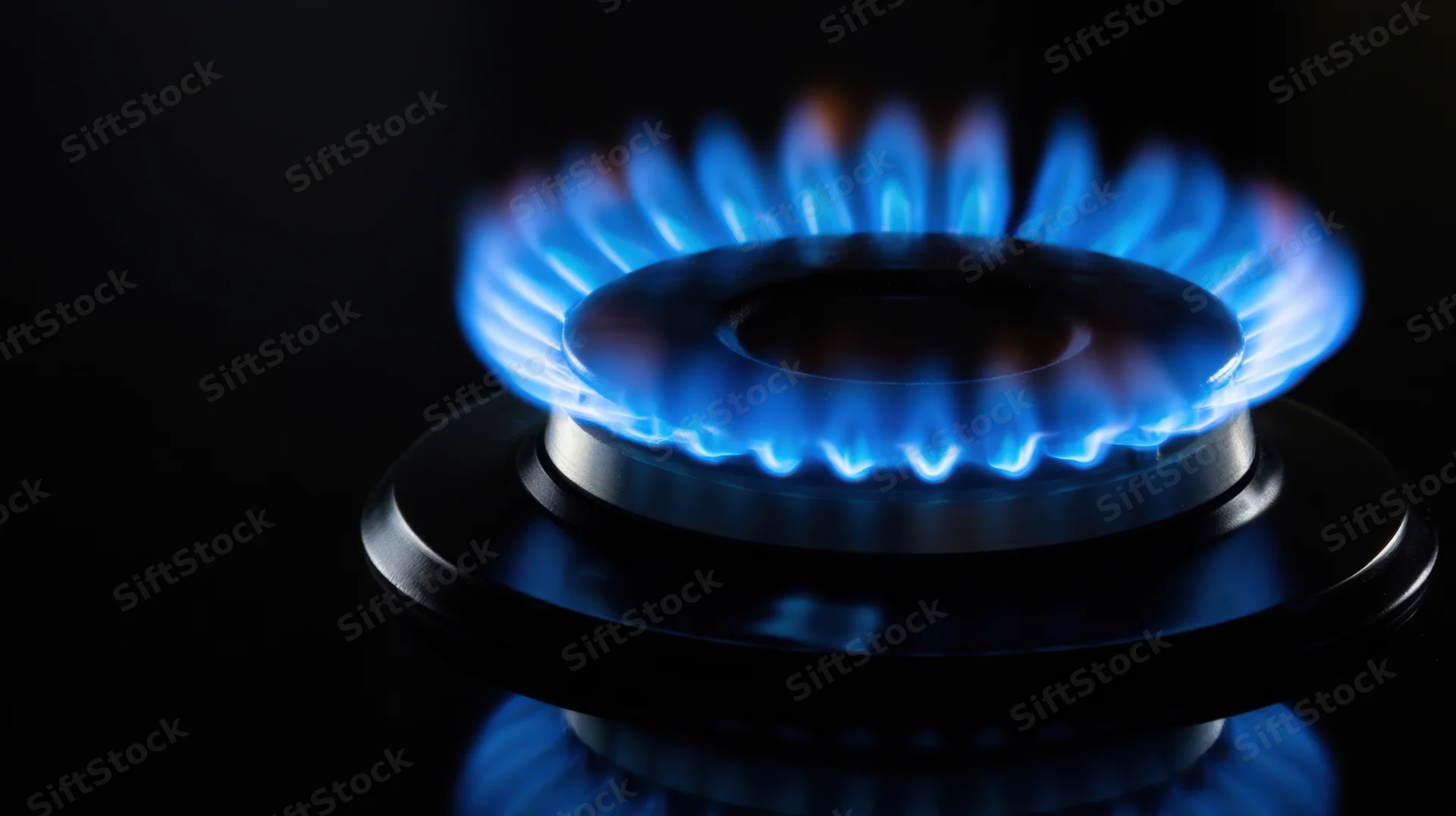 Lit gas stove burner with blue flame on dark background
