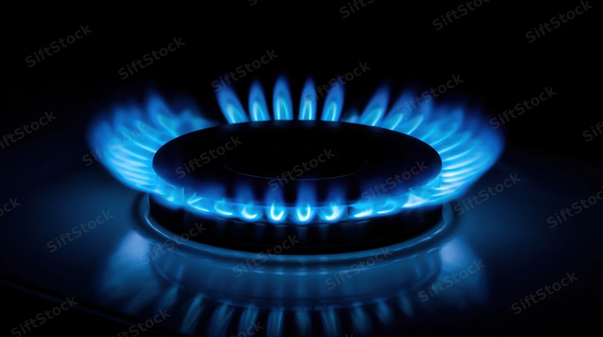 Blue flame burning on a gas stove burner in a dark kitchen setting