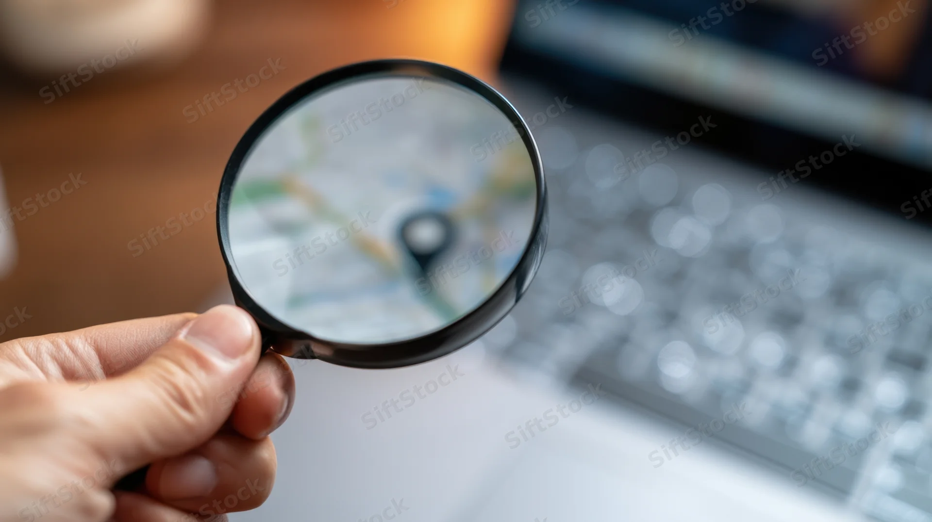 Hand holding magnifying glass over digital map on laptop screen in office workspace