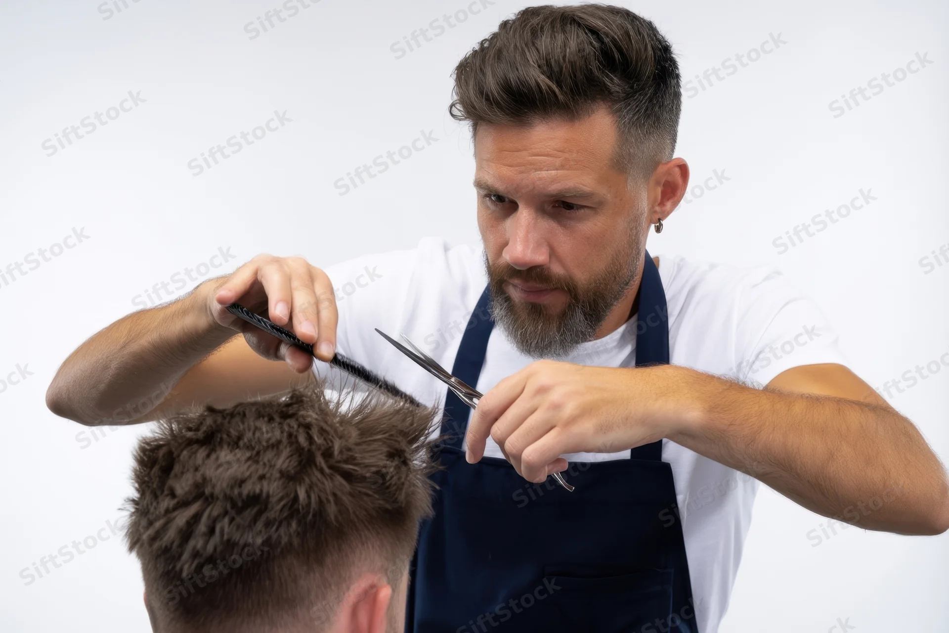 Barber cutting a man's hair with scissors and comb in a studio setting