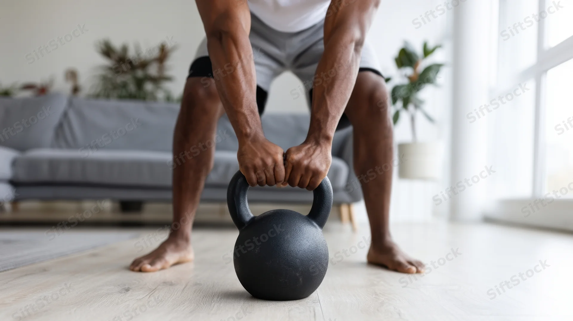 Man lifting kettlebell barefoot in living room during home workout
