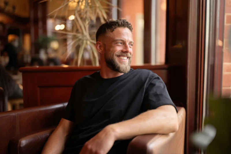Man smiling while seated on a leather couch in a cafe interior