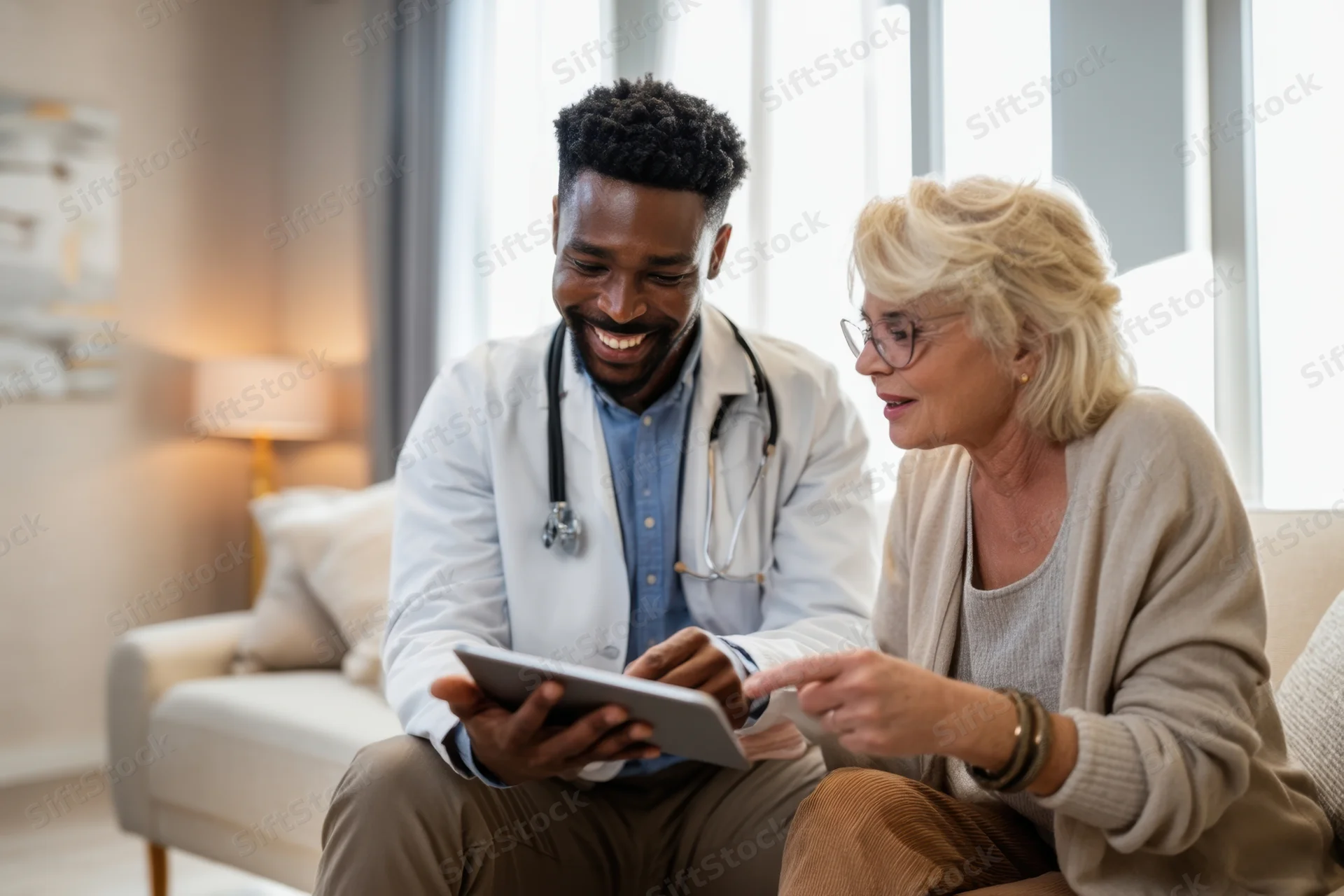 Doctor and senior woman discussing medical information on tablet during home visit