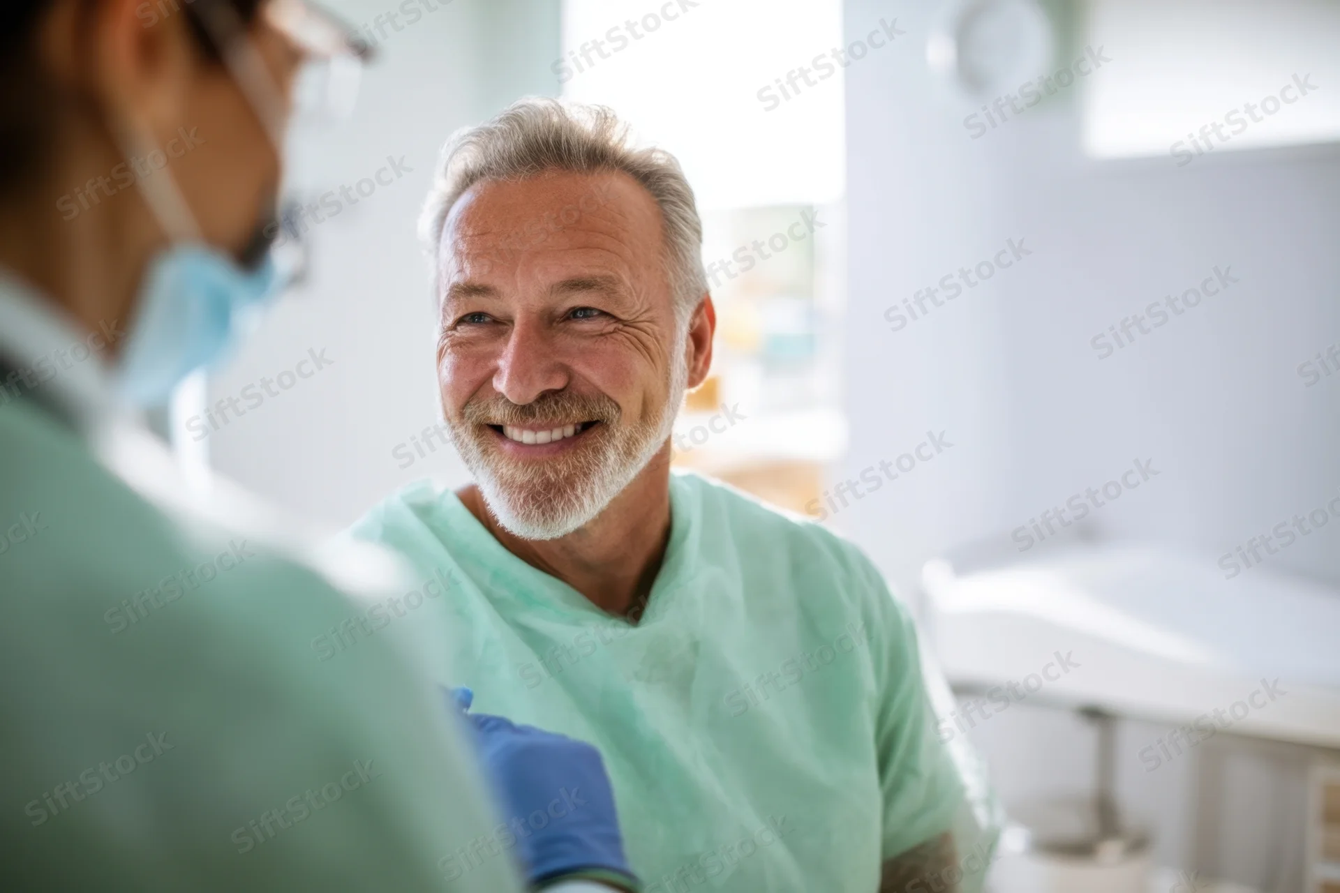 Senior man smiling during medical consultation in clinic with doctor in scrubs