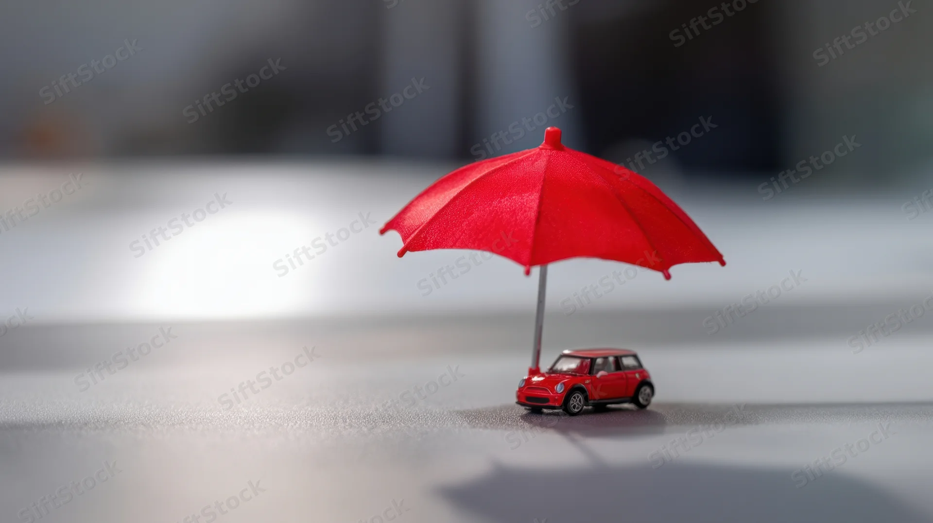 Red miniature car under a red umbrella on a gray surface