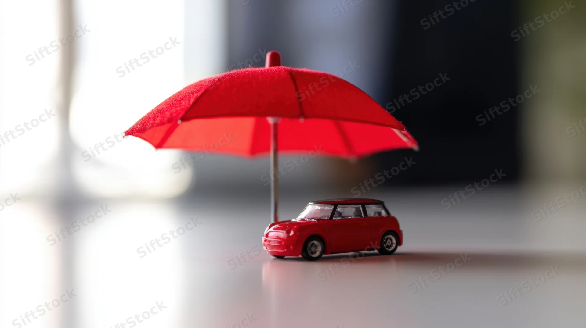 Red toy car under a red umbrella on a smooth surface