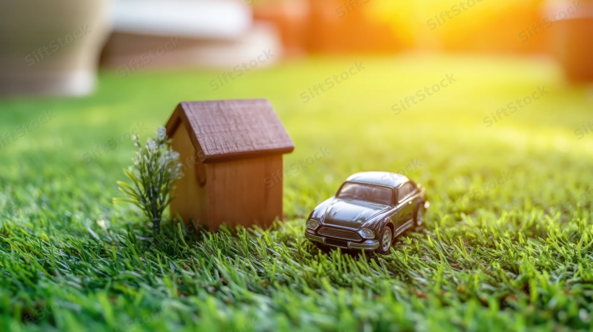 Miniature house and car on a grassy lawn in sunlight