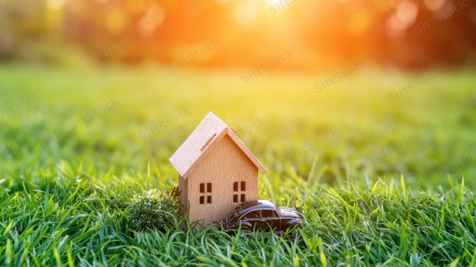 Miniature wooden house and toy car on green grass at sunset