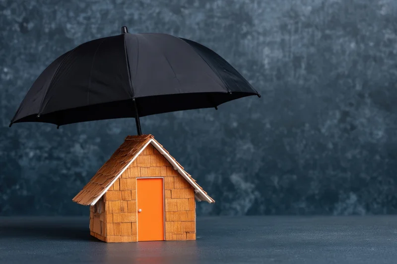 Miniature wooden house with orange door under black umbrella on textured blue surface