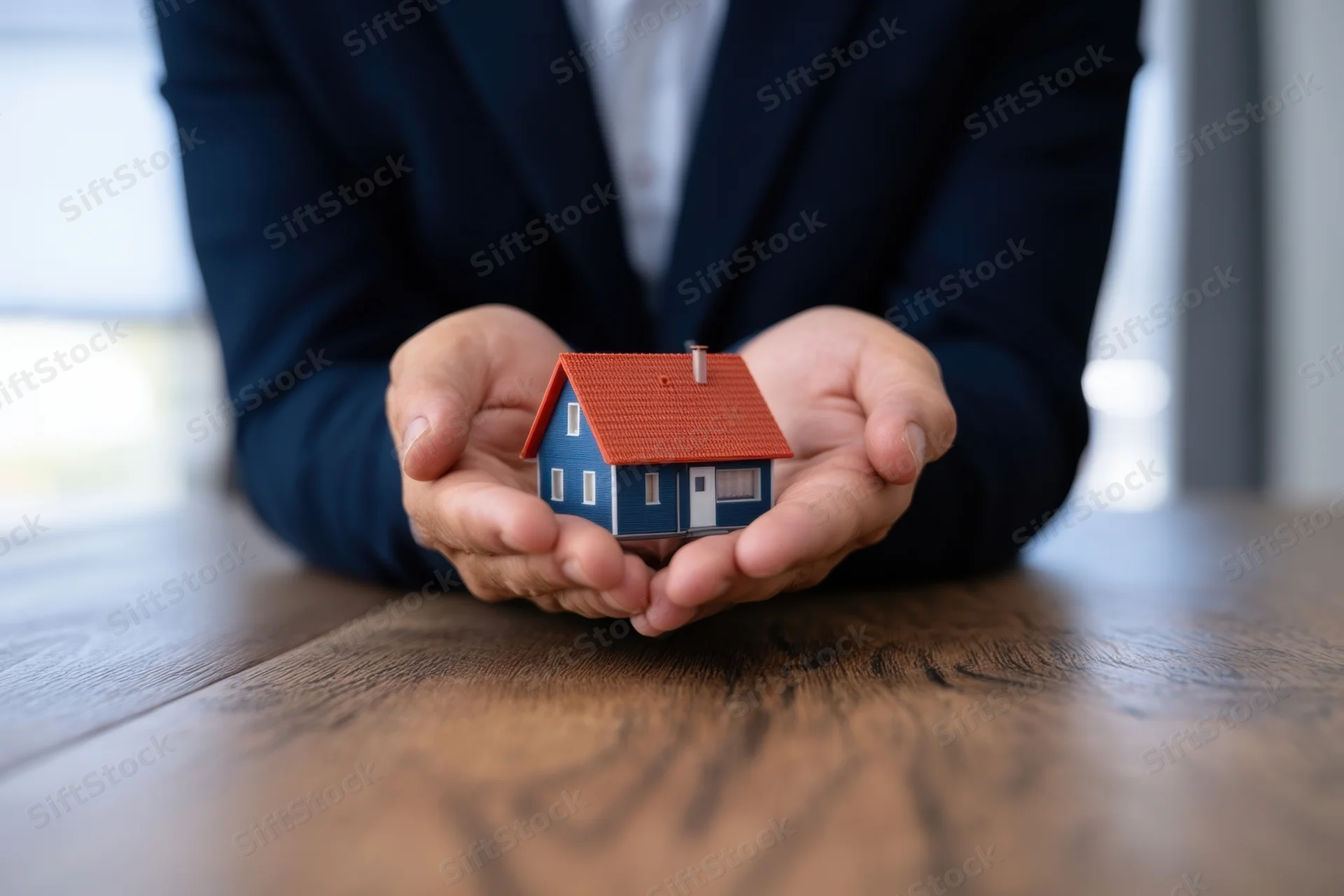 Businessman holding miniature house model on wooden desk