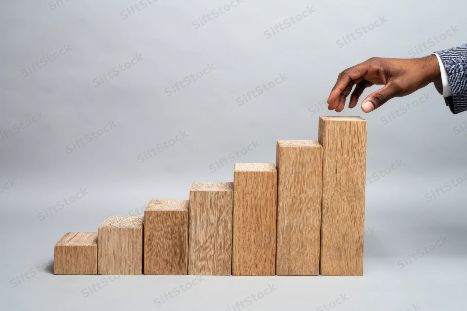 Hand placing wooden block on ascending bar chart in studio setting