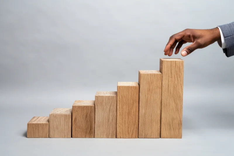 Hand placing wooden block on ascending bar chart in studio setting