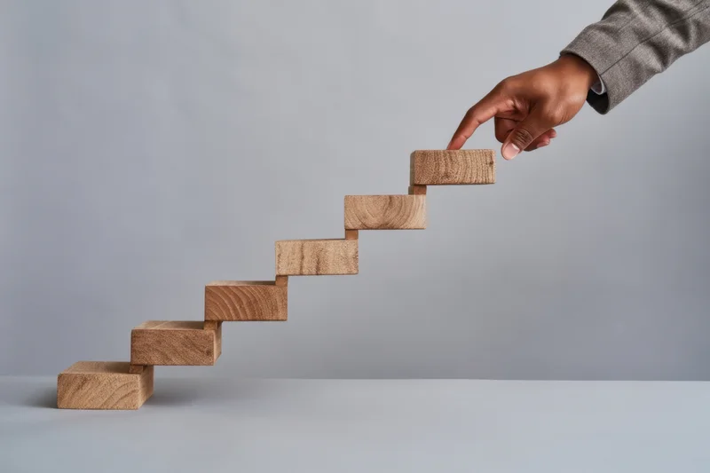 Hand placing wooden block on ascending staircase on gray surface