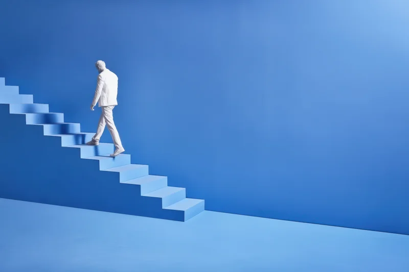 Man in white suit climbing blue staircase in minimalist setting