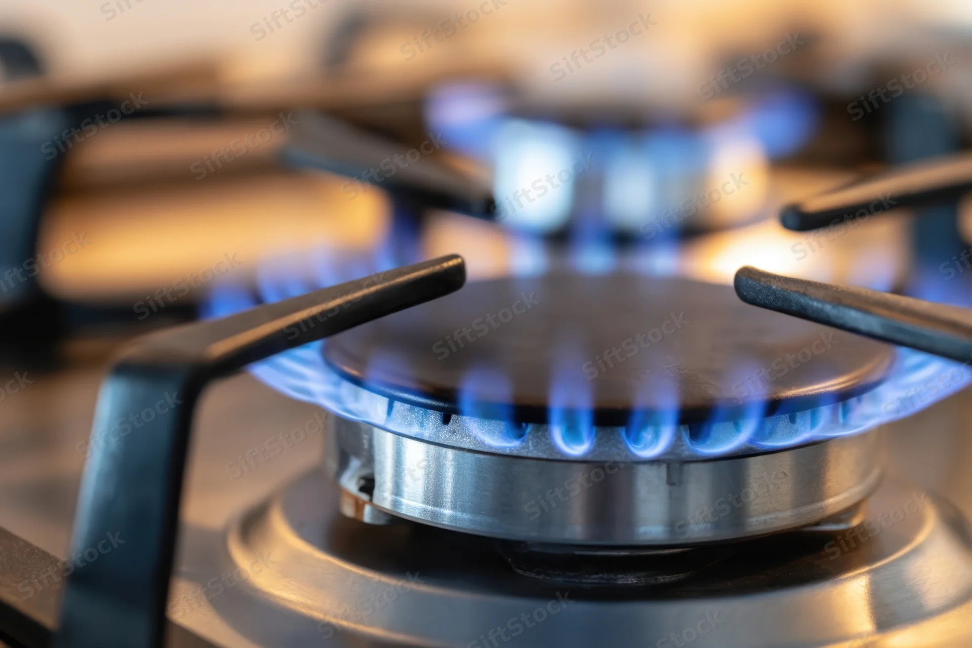 Close-up of a lit gas stove burner with blue flames on a modern cooktop