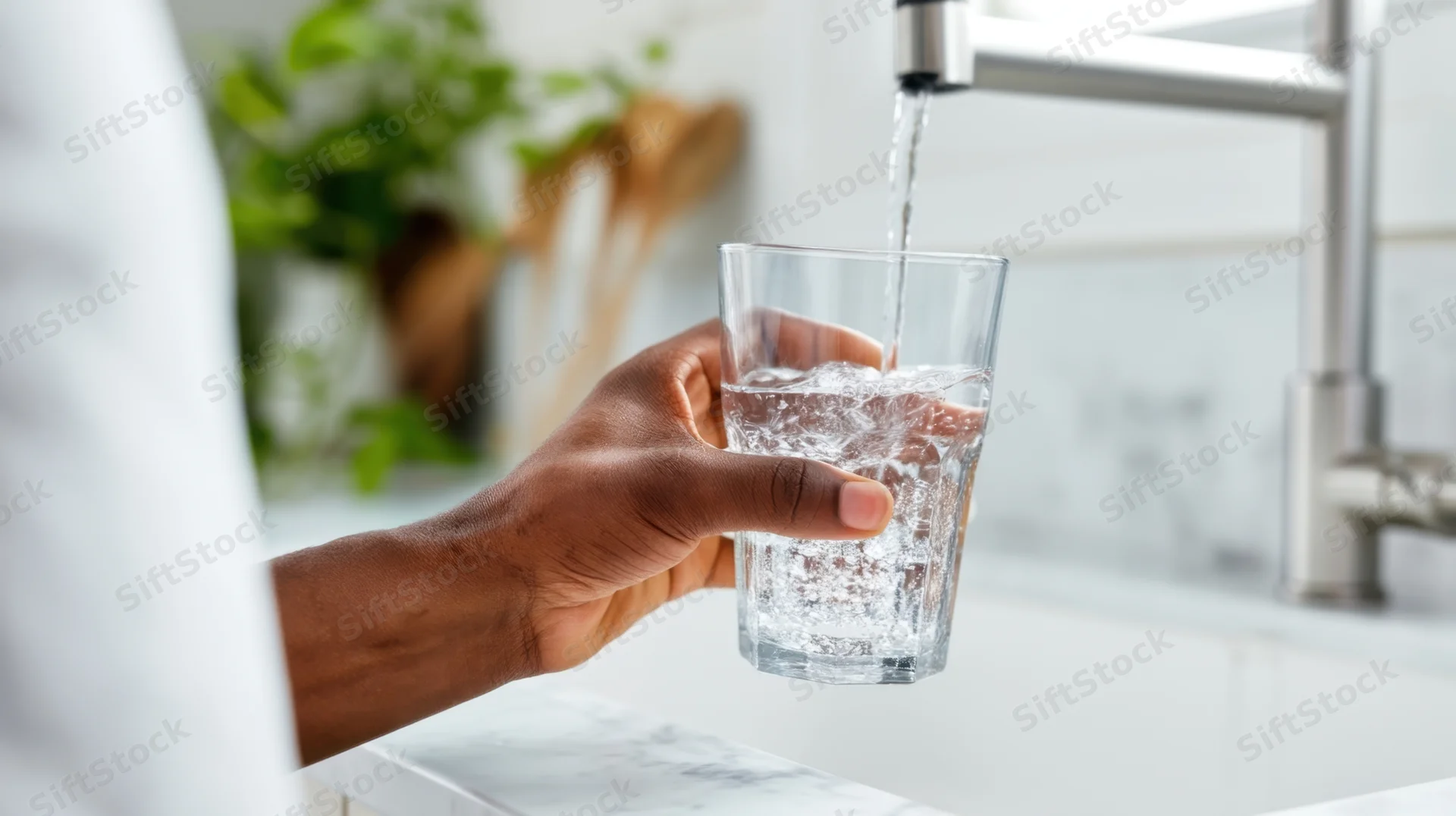 Hand holding a glass under running tap water in a modern kitchen sink