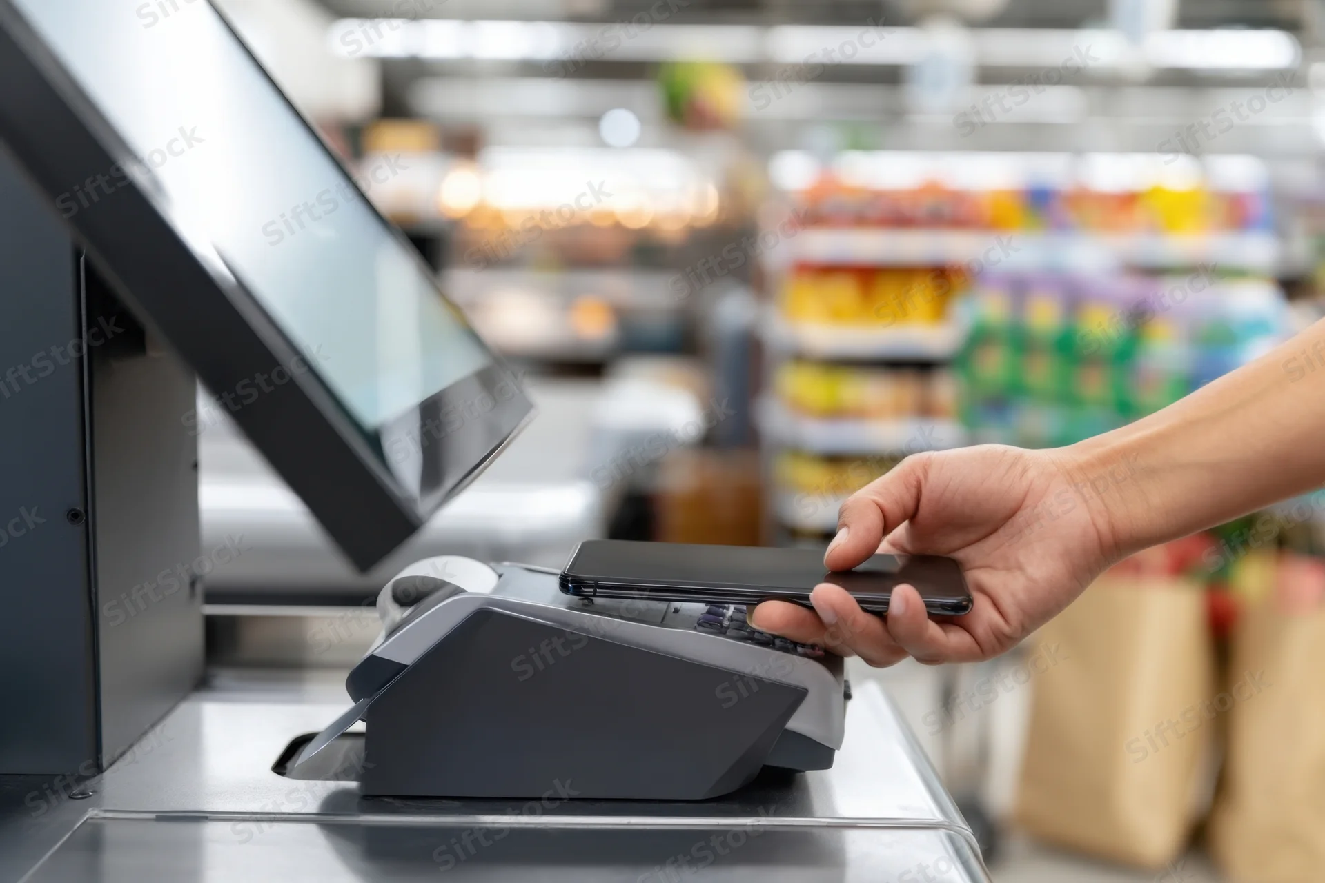 Hand tapping smartphone on payment terminal at supermarket checkout