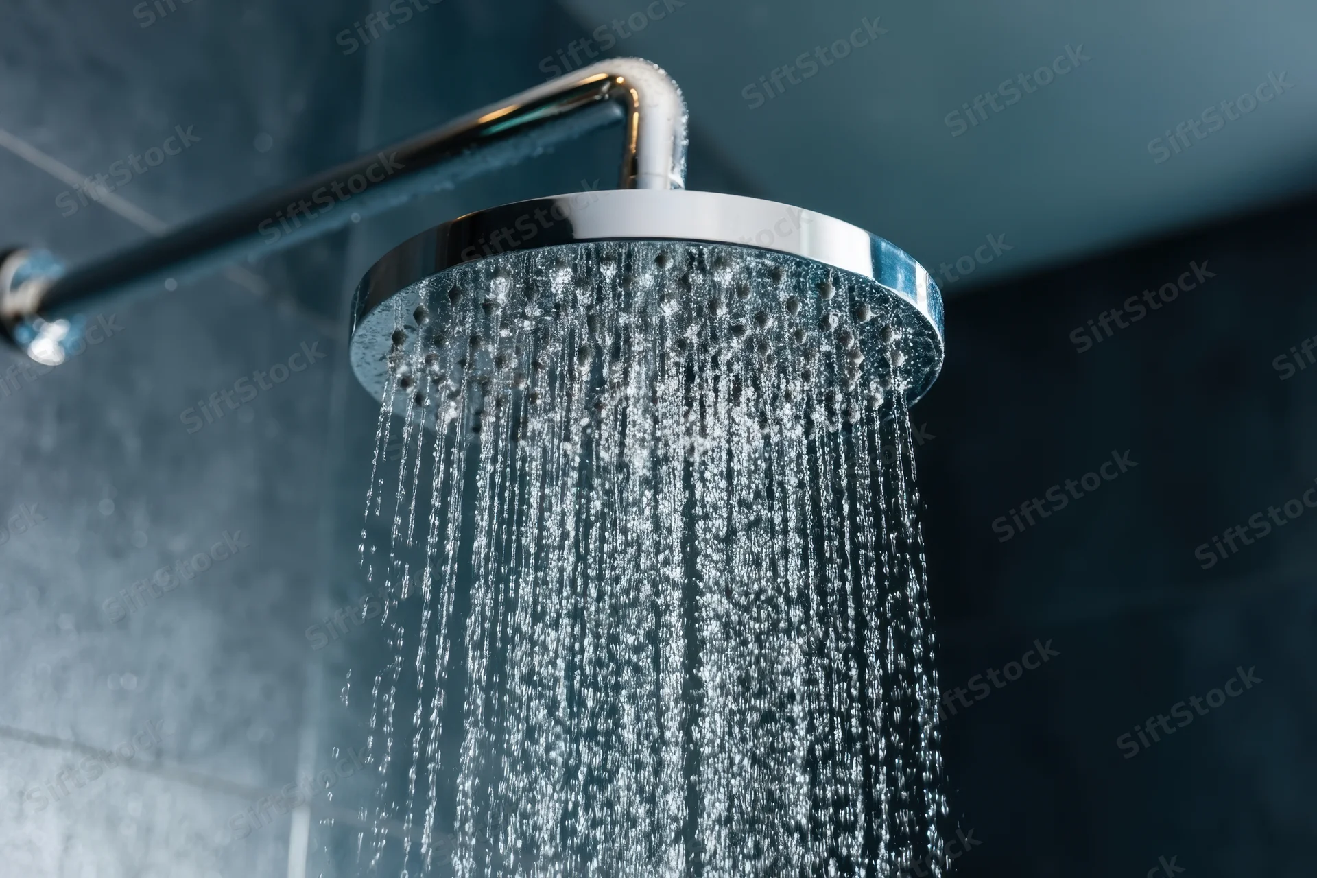 Modern chrome showerhead spraying water in a gray tiled bathroom