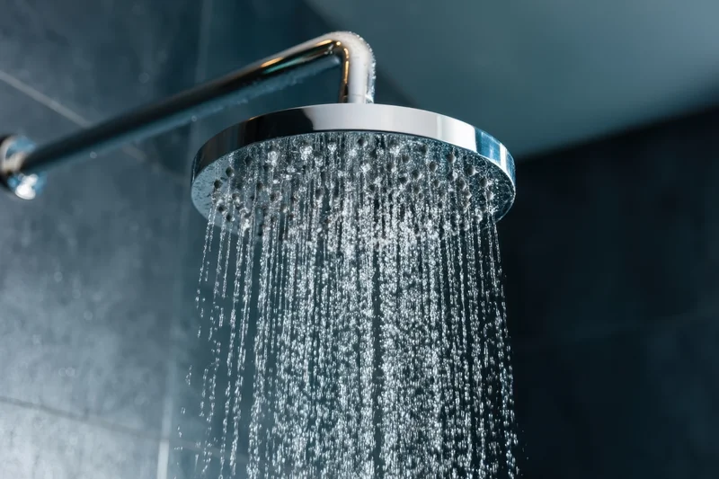 Modern chrome showerhead spraying water in a gray tiled bathroom