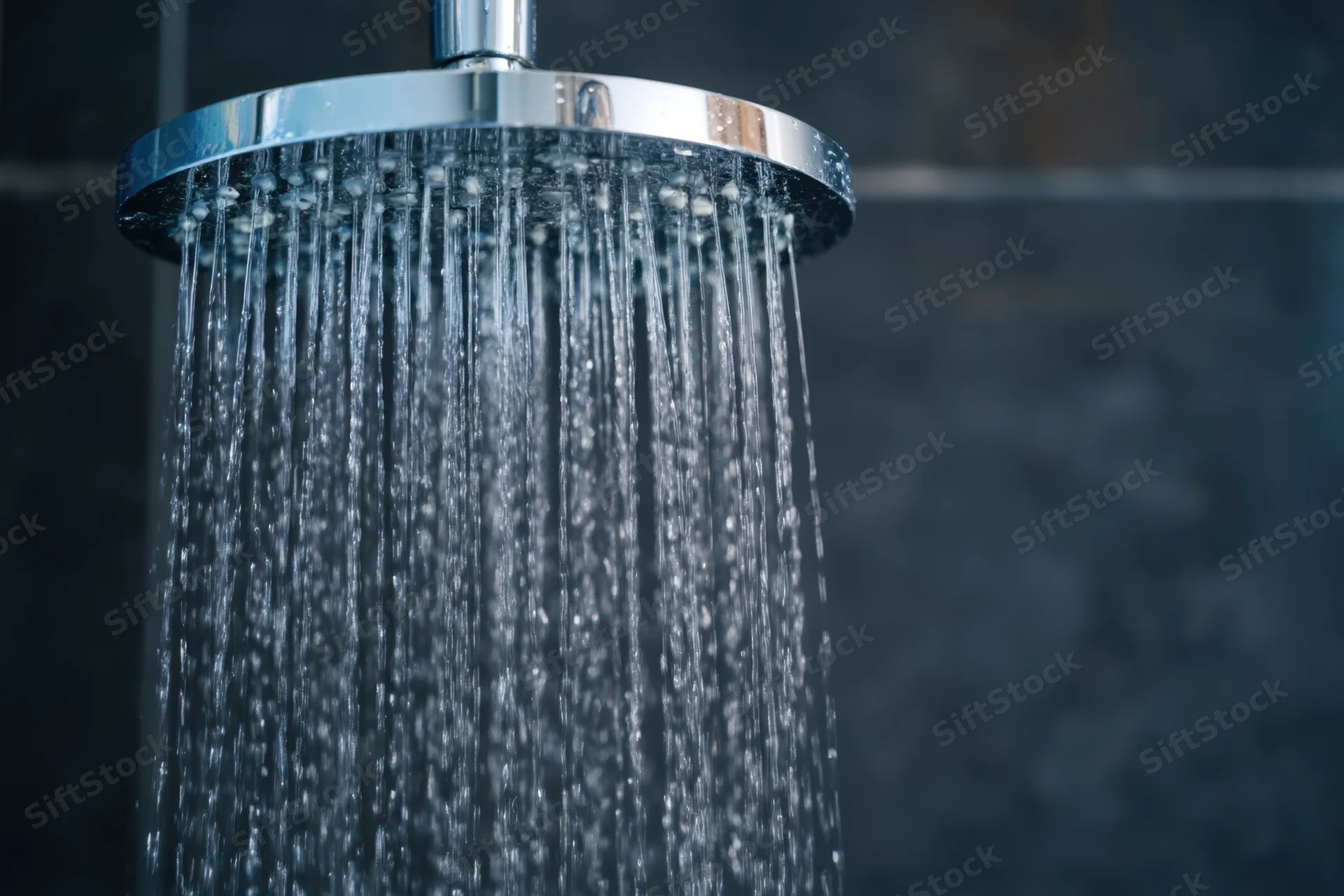 Close-up of a modern chrome showerhead spraying water in a dark tiled bathroom