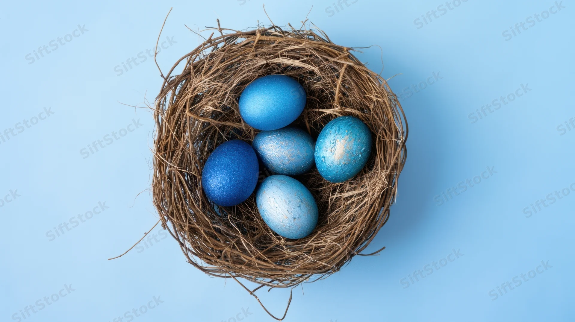 Blue painted eggs in a natural twig nest on a light blue background