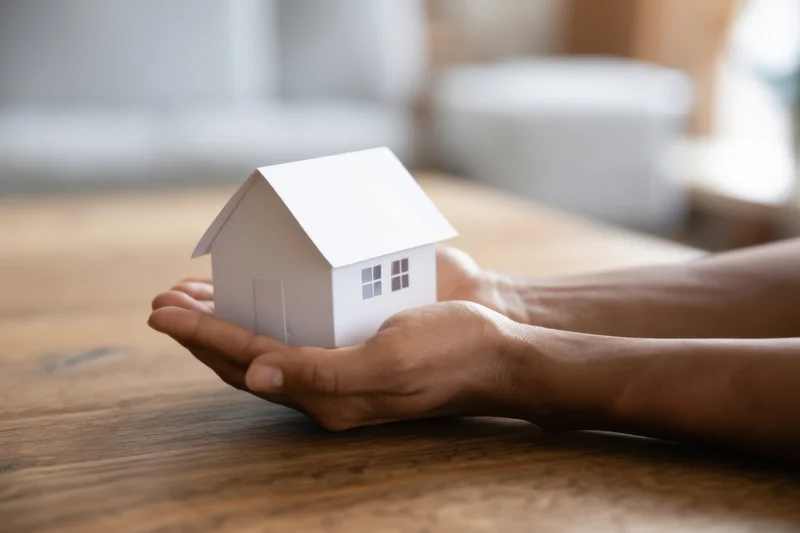 Woman's hands holding a white paper house model on a wooden table