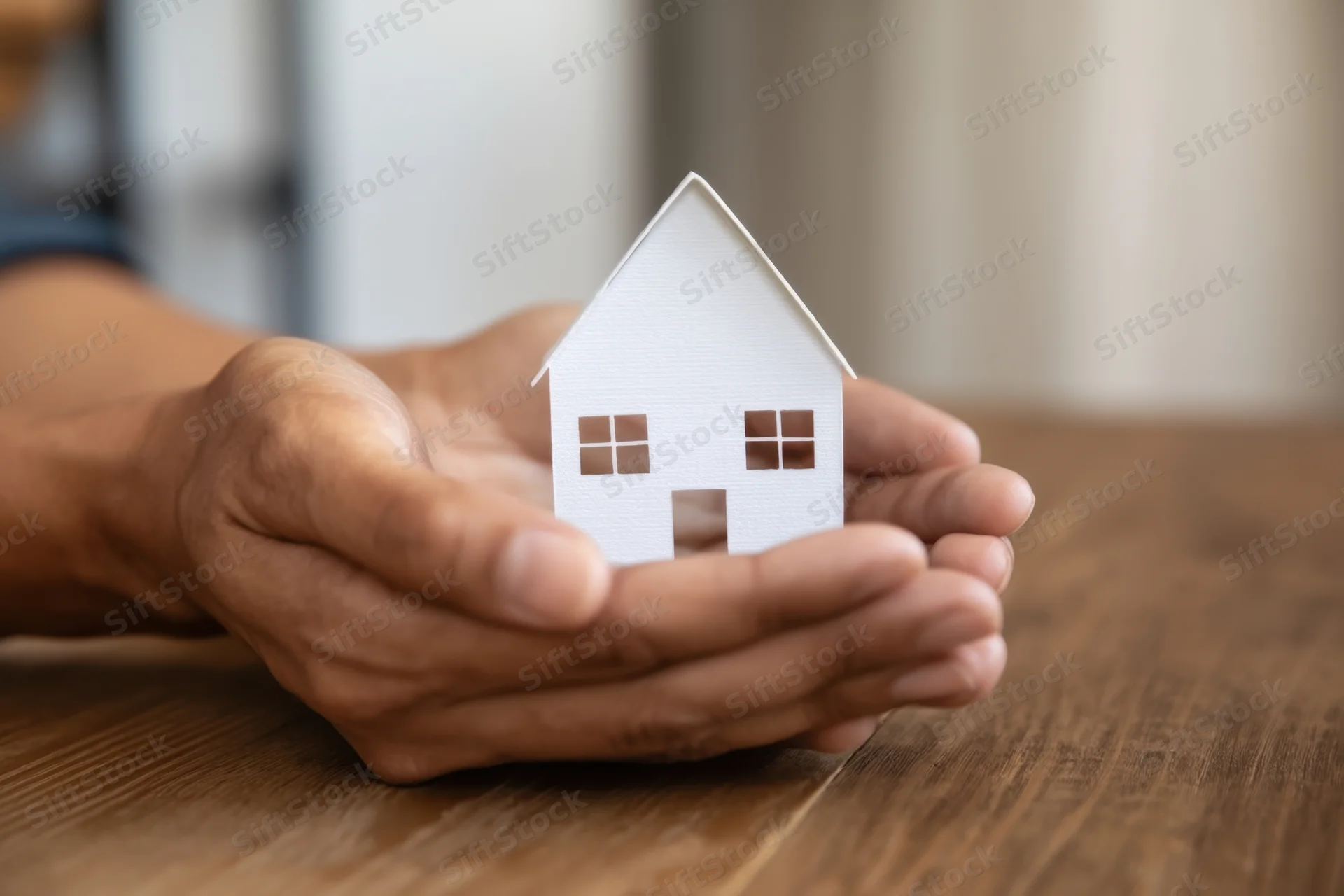 Hands holding a white paper house model on a wooden table