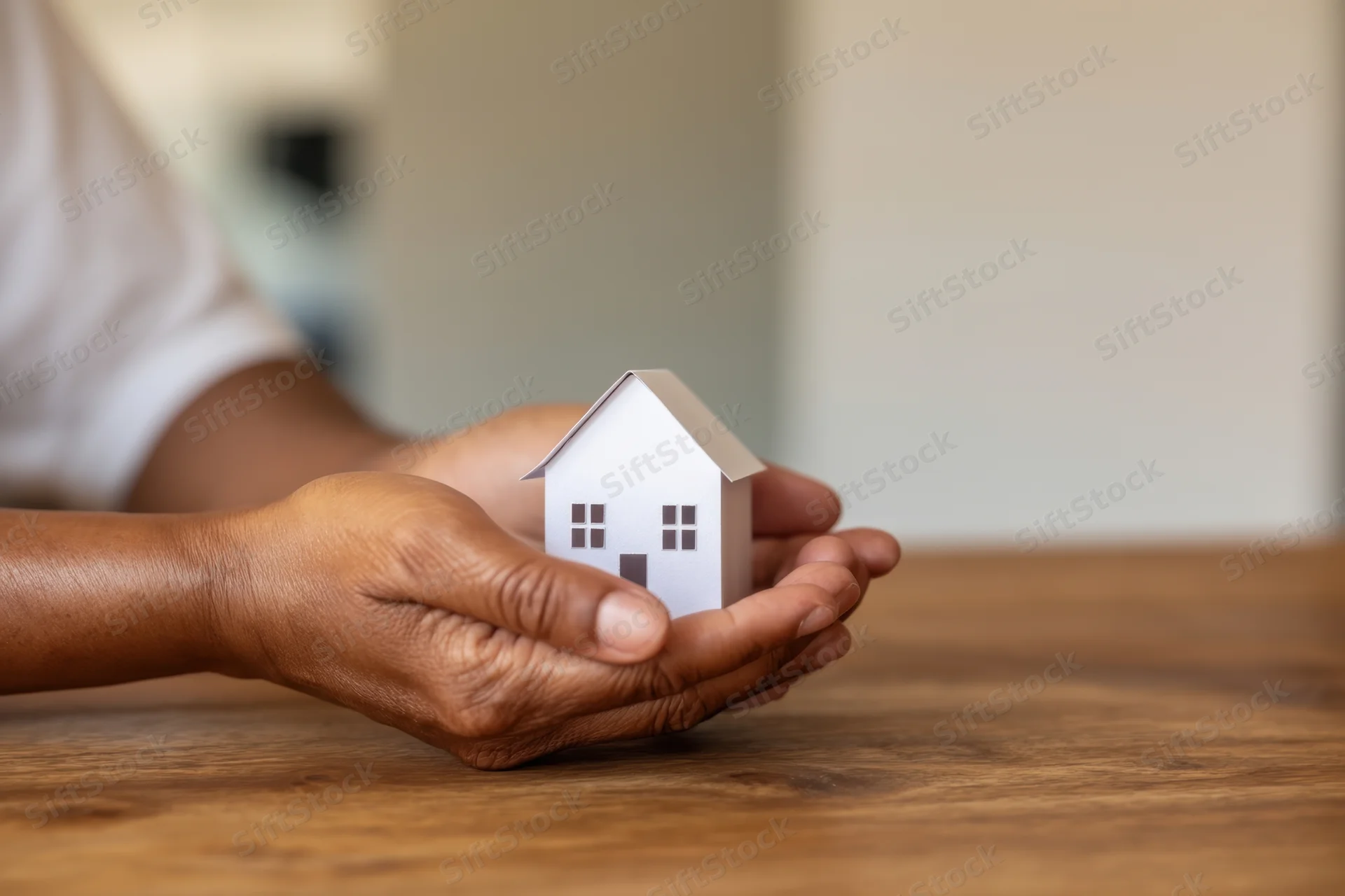 Woman's hands holding a small white house model on a wooden table