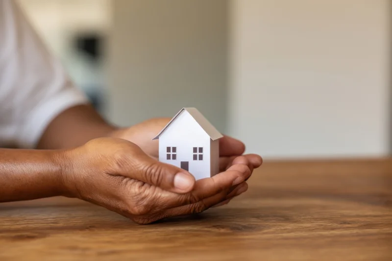 Woman's hands holding a small white house model on a wooden table