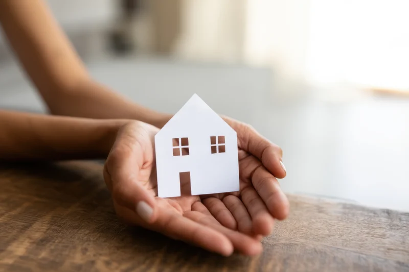 Woman's hands holding a white paper house cutout on a wooden table