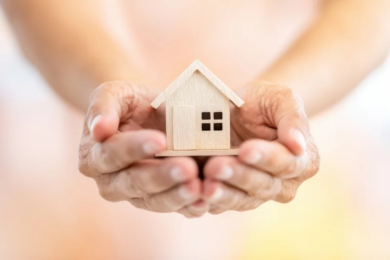Hands cradling a small wooden house model against a soft blurred background