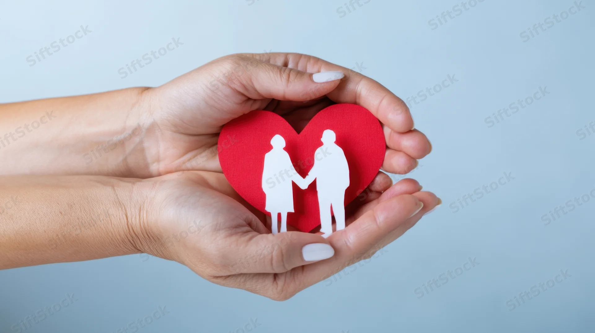 Hands holding a red heart with white couple cutout against light blue background