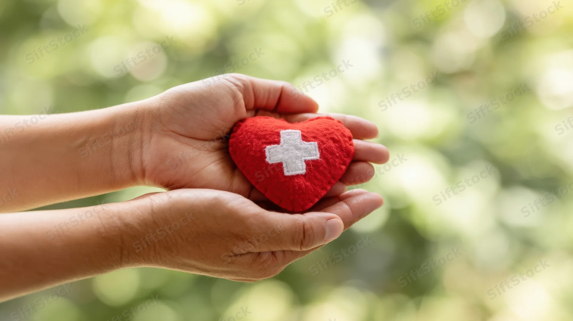 Hands holding a red felt heart with white cross symbol outdoors