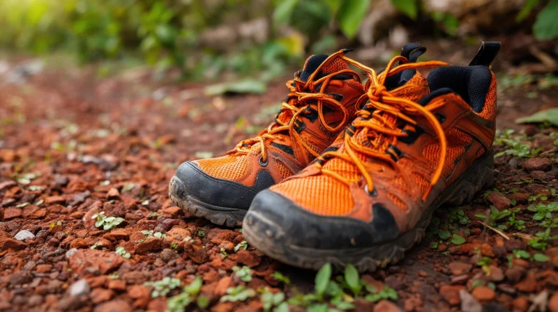 Orange hiking boots resting on a dirt path surrounded by green foliage