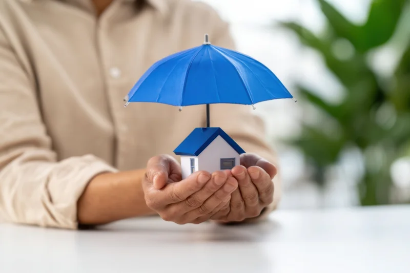 Woman holding miniature house under blue umbrella on desk
