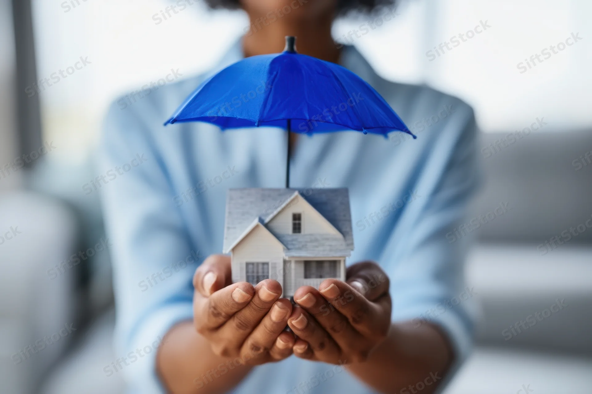 Woman holding a miniature house under a blue umbrella indoors