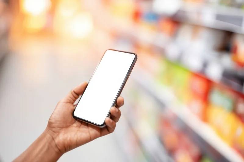 Hand holding smartphone with blank screen in grocery store aisle