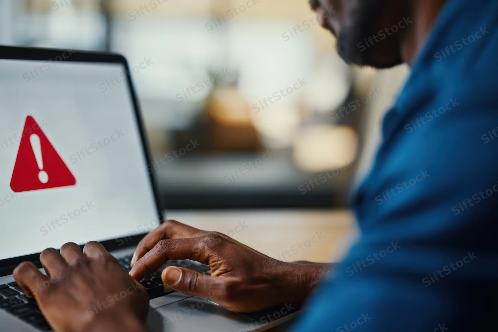Man typing on laptop with warning symbol on screen in office setting