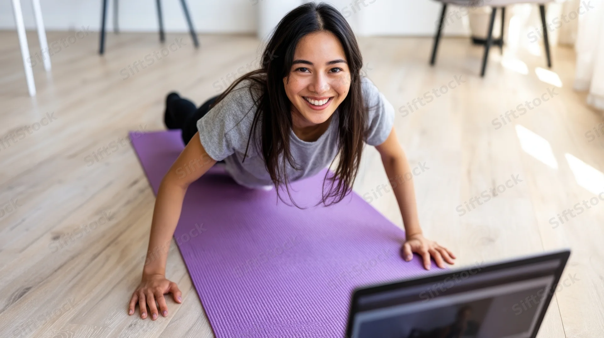 Woman doing plank exercise on purple mat in front of laptop at home