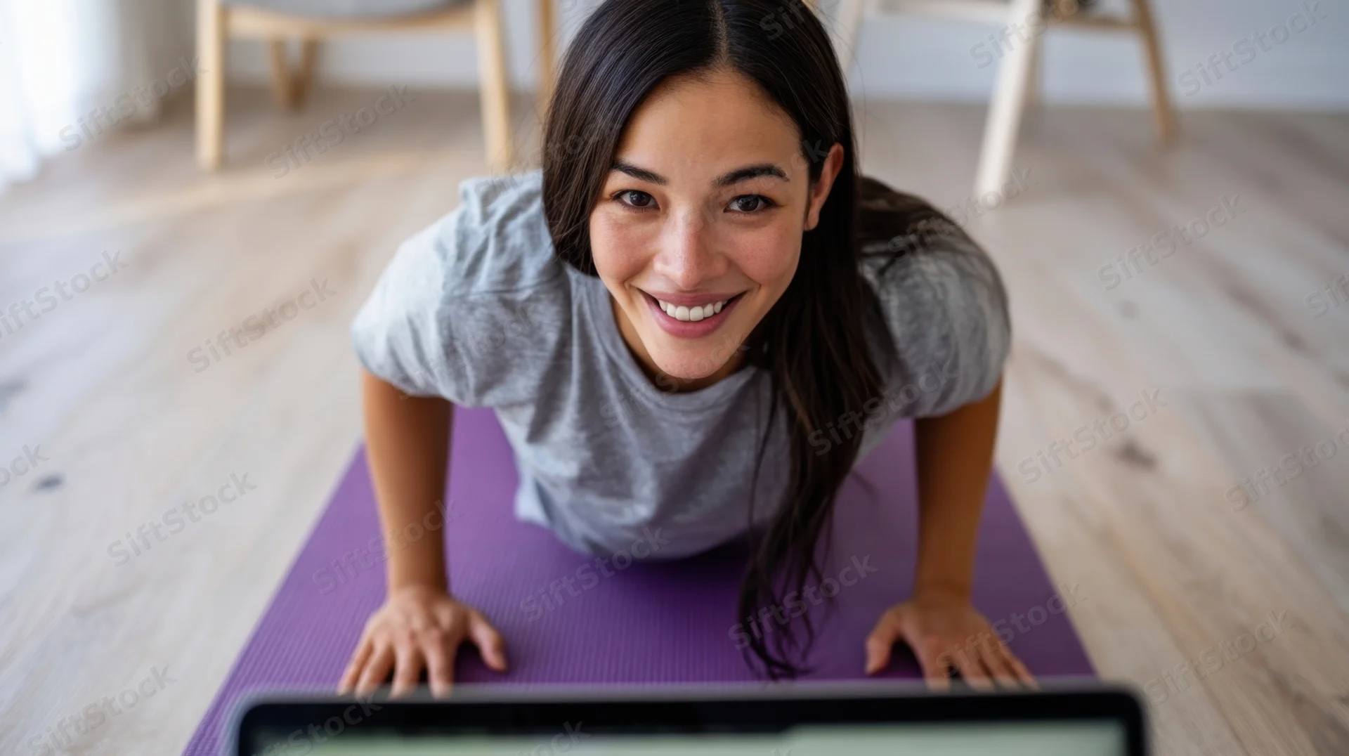 Woman doing pushup on yoga mat at home while smiling at laptop screen