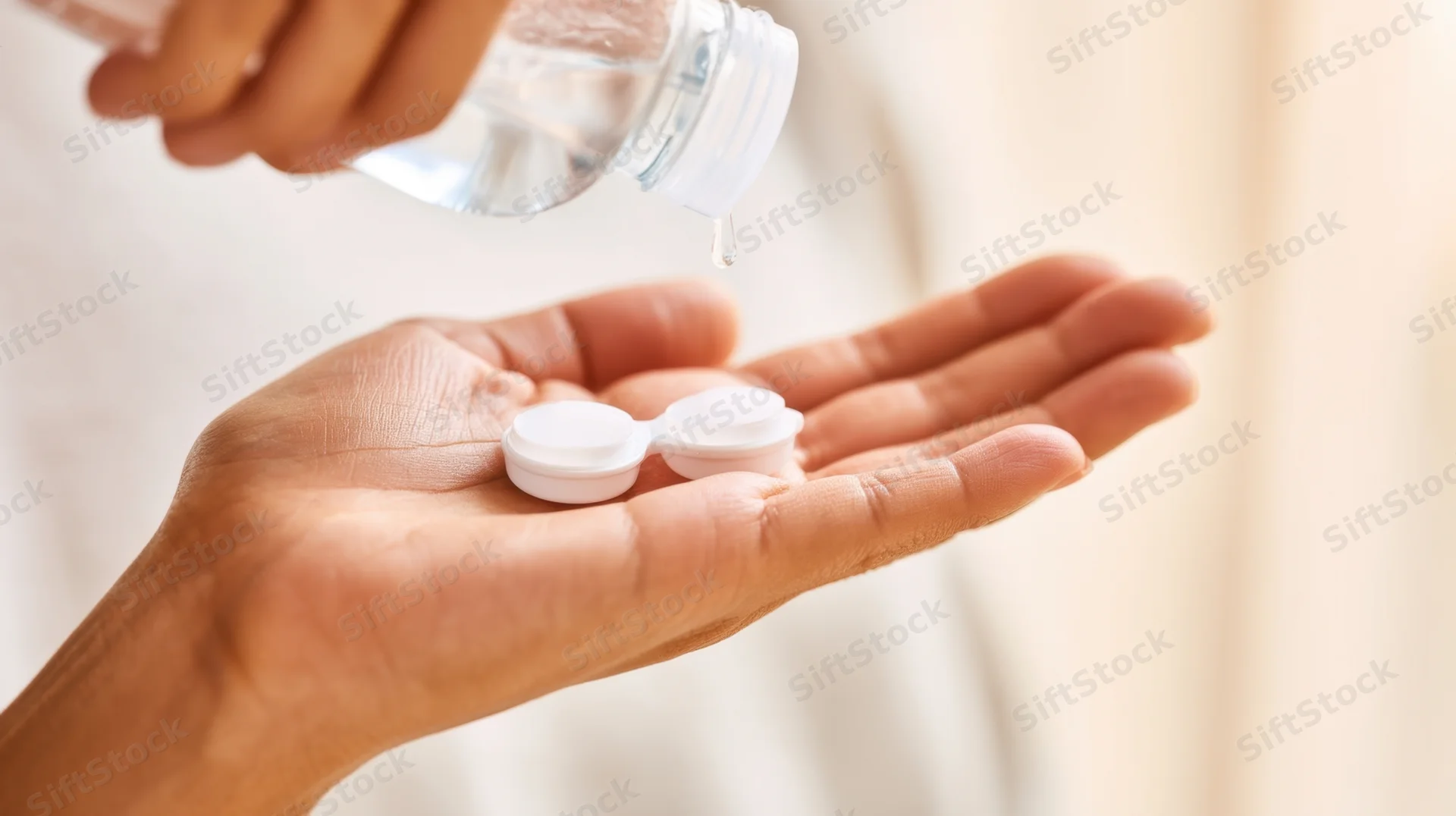 Hand holding contact lenses with cleaning solution being poured from a bottle