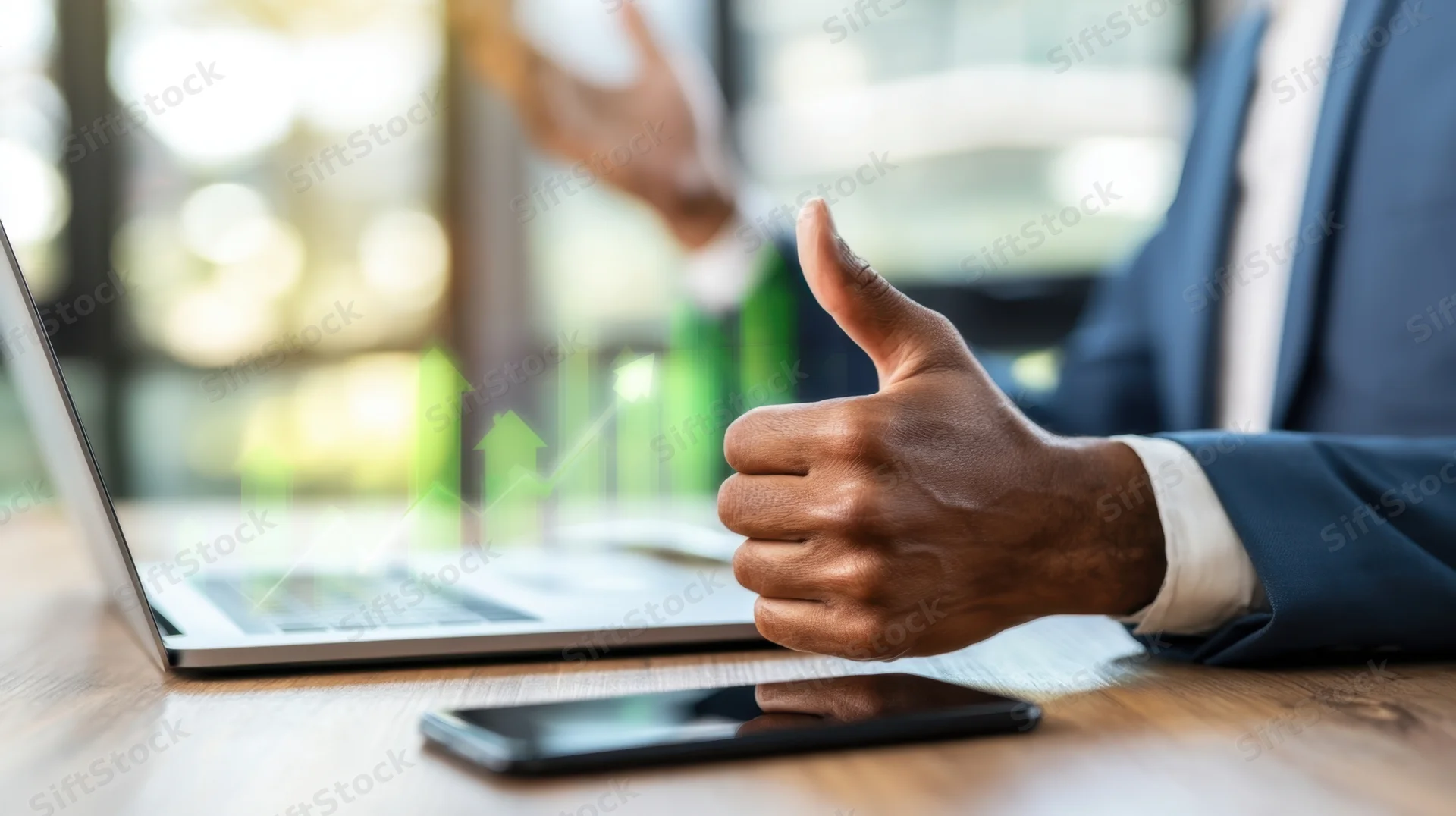 Man in suit giving thumbs up at laptop with green growth chart on wooden desk in office