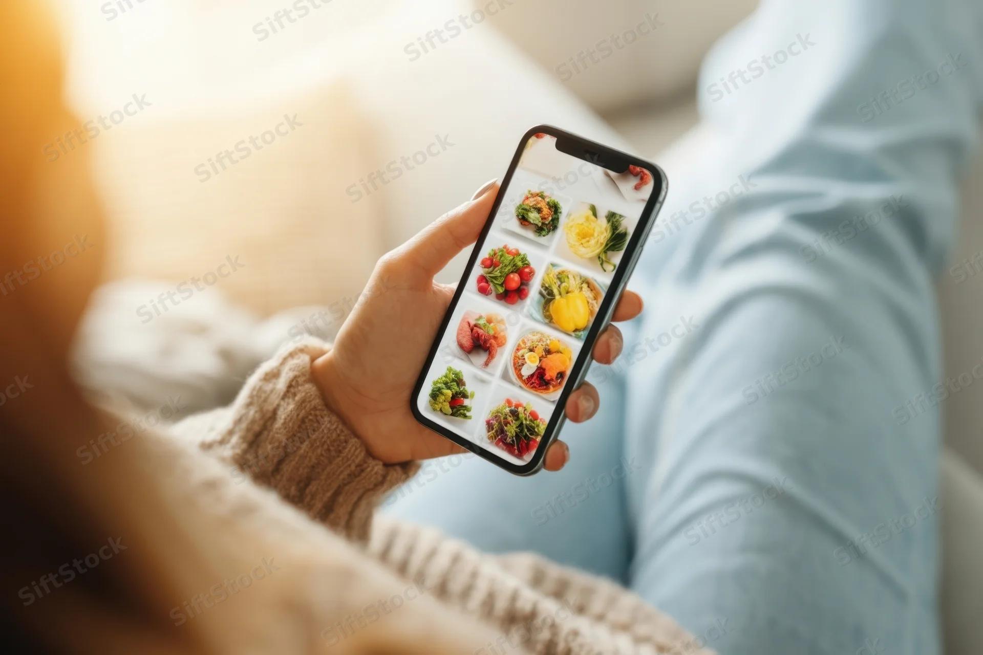 Woman holding smartphone displaying food app grid while relaxing at home