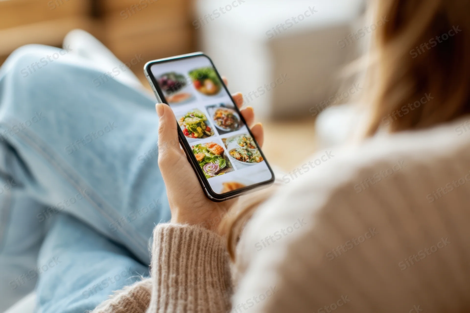 Woman browsing food delivery app on smartphone while sitting on couch at home