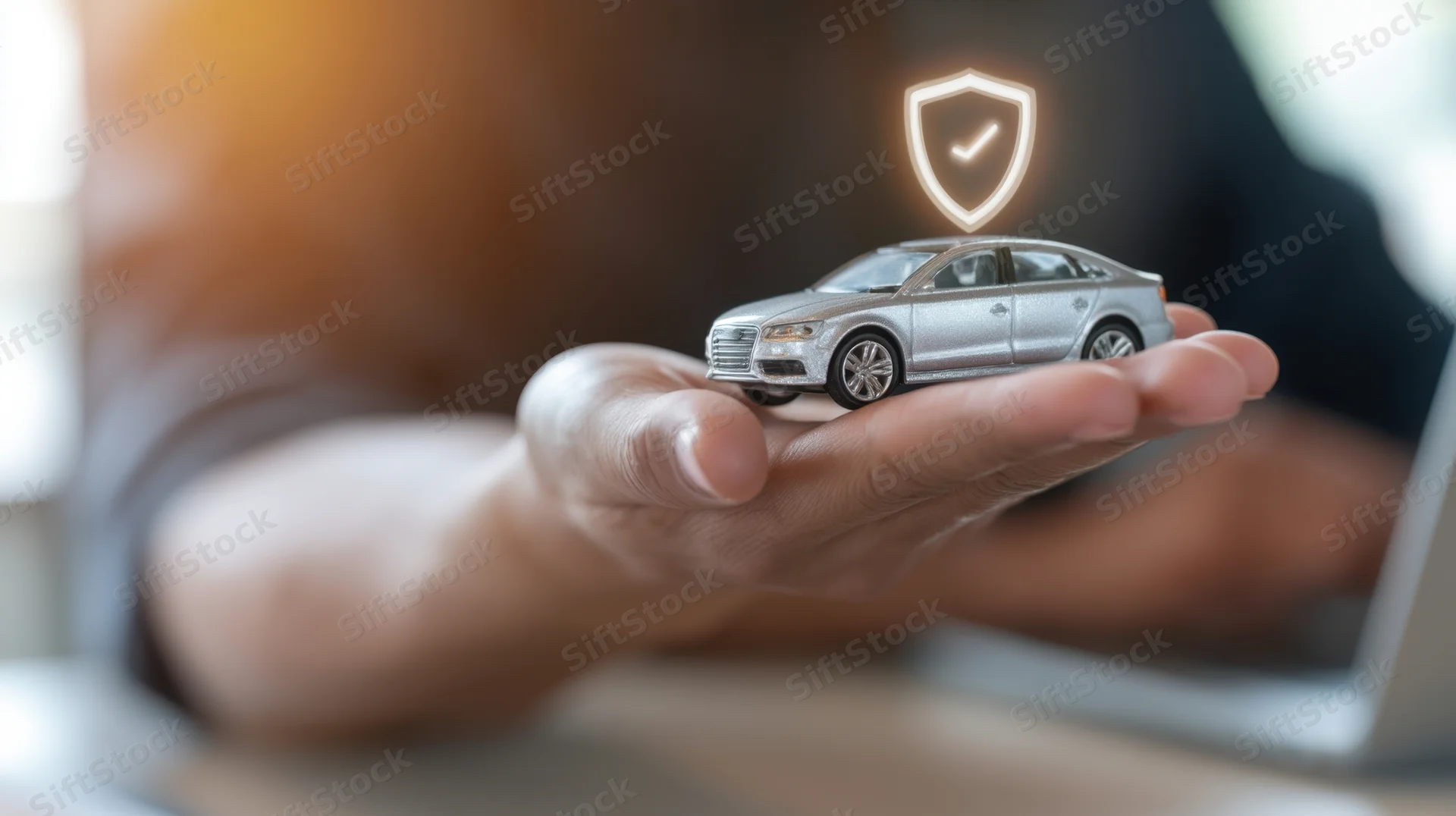 Hand holding a silver toy car with a glowing shield hologram above it at a desk