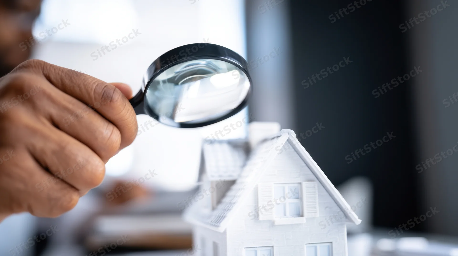 Hand holding magnifying glass over white house model on desk