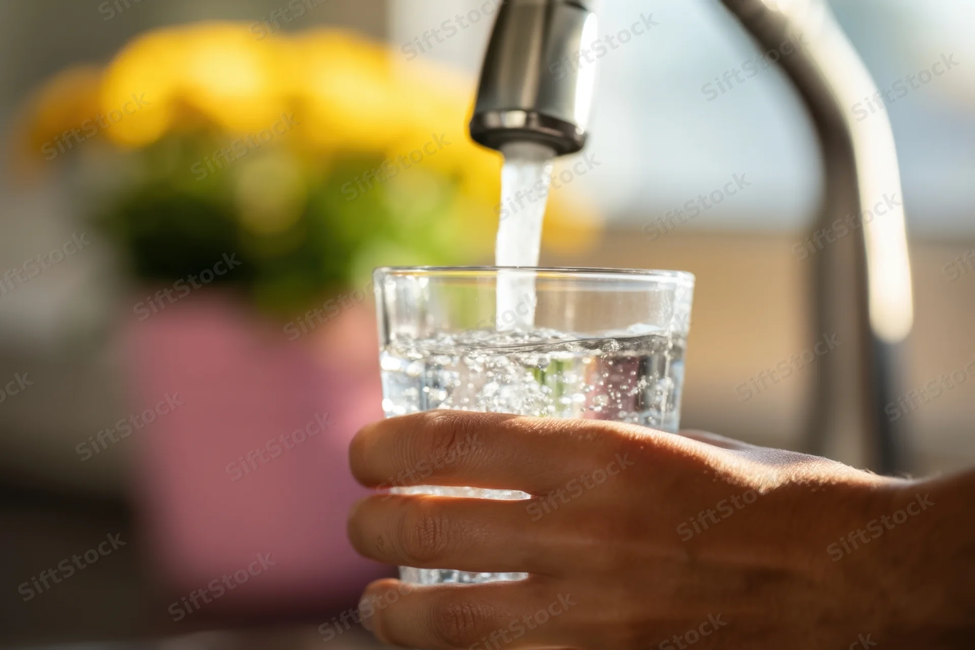 Hand holding a glass under running tap water in a kitchen